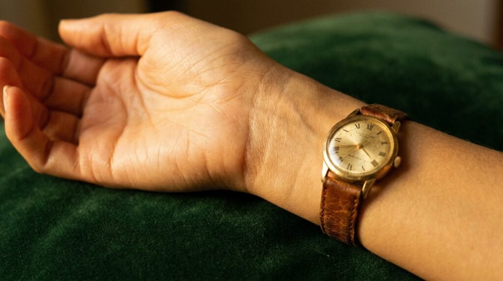 Smooth luminous skin on wrist with vintage gold watch on dark green velvet