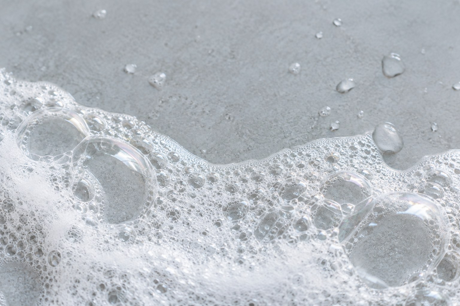 Airy cleanser bubbles and clear water droplets on a pale grey surface.