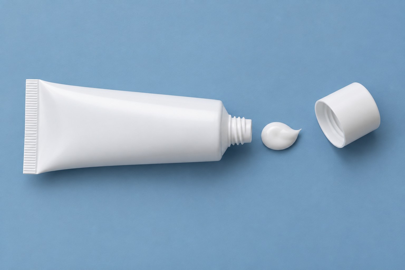 An unlabelled white tube and a small dab of cream on a blue surface.
