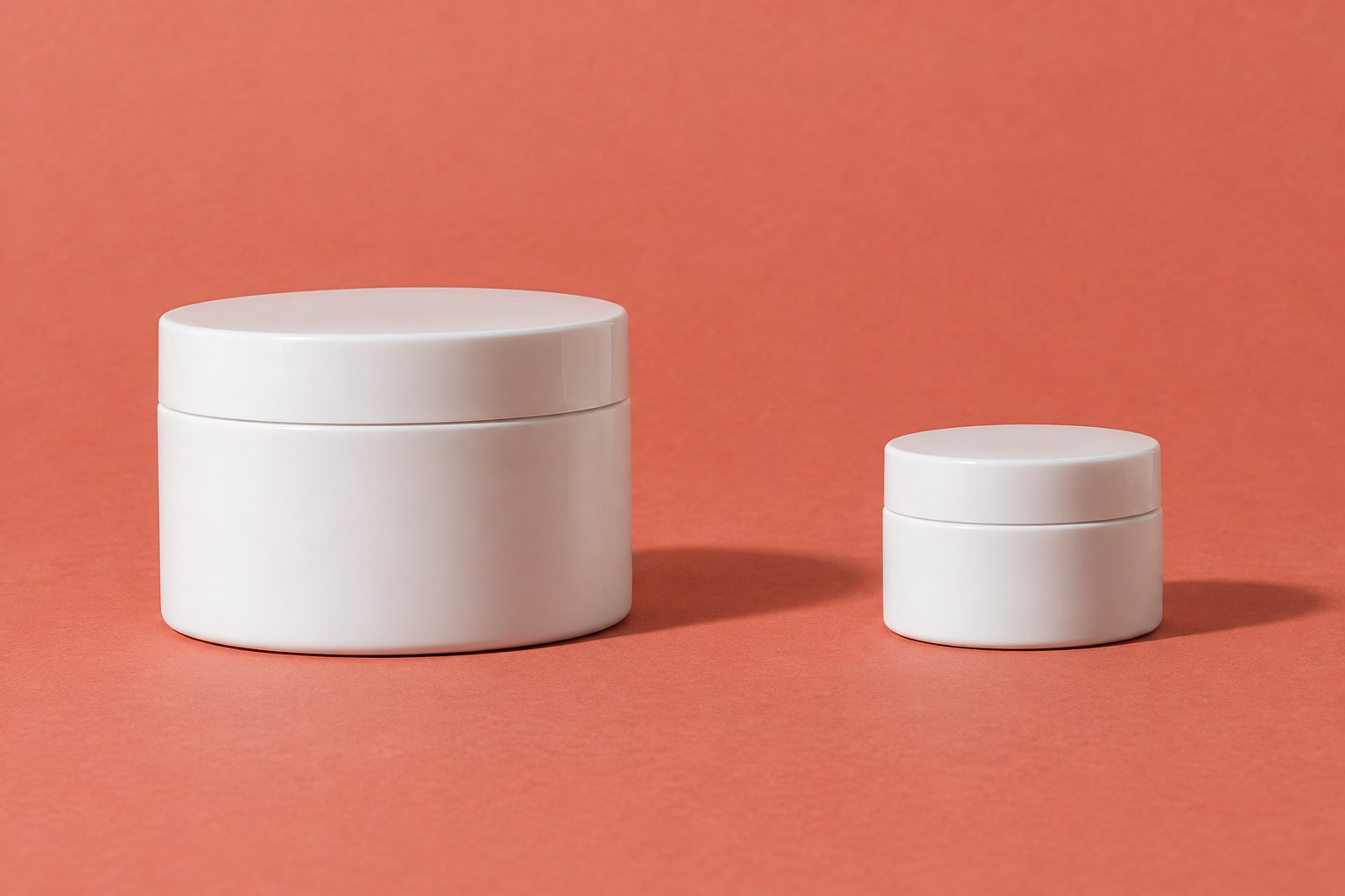 Large and small unlabelled white cream jars on a coral background.